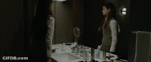 A Woman Stands In Front Of A Bathroom Mirror GIF