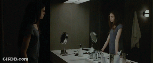 A Woman Stands In Front Of A Bathroom Mirror Looking At Herself GIF