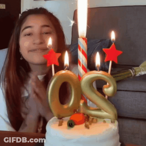 A Woman Stands In Front Of A Birthday Cake With Candles In The Shape Of The Number Two GIF