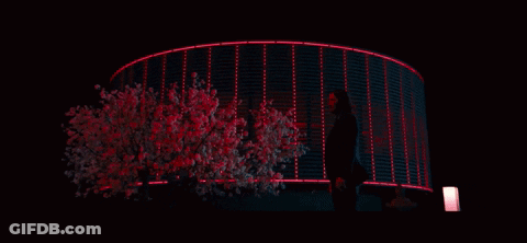 A Woman Stands In Front Of A Building That Is Lit Up With Red Lights GIF