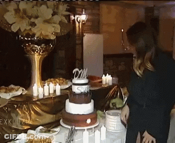 A Woman Stands In Front Of A Cake With A Topper That Says Dm On It GIF