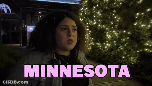 A Woman Stands In Front Of A Christmas Tree With The Word Minnesota On The Bottom GIF