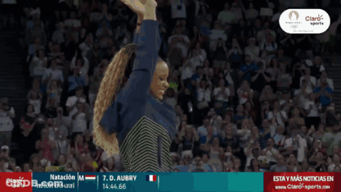 A Woman Stands In Front Of A Crowd With Her Arms In The Air And A Banner That Says Natacion GIF