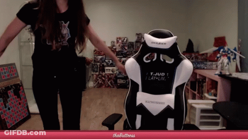 A Woman Stands In Front Of A Gaming Chair That Says T. Jud I Lay-Liv GIF