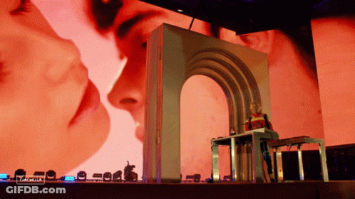 A Woman Stands In Front Of A Large Screen That Says " Coachella " On It GIF