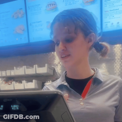 A Woman Stands In Front Of A Mcdonald 'S Checkout Counter With A Menu Behind Her GIF