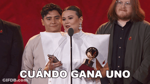 A Woman Stands In Front Of A Microphone Holding A Trophy And The Words Cuando Gana Uno Behind Her GIF