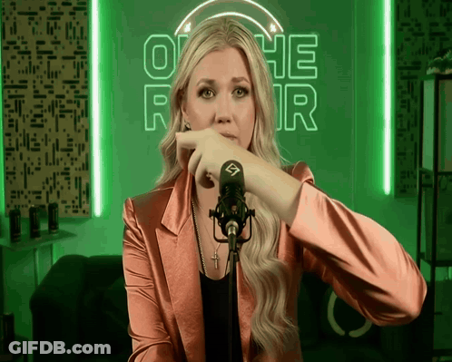 A Woman Stands In Front Of A Microphone In Front Of A Neon Sign That Says Othe R GIF