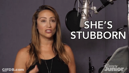 A Woman Stands In Front Of A Microphone With The Words She 'S Stubborn Behind Her GIF