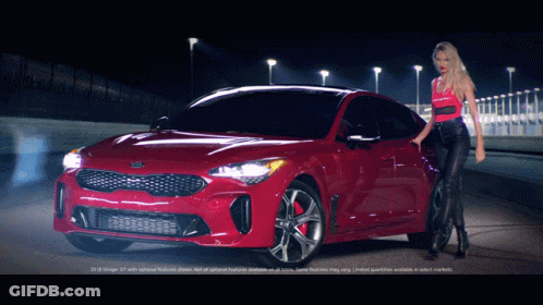 A Woman Stands In Front Of A Red Kia Stinger GIF