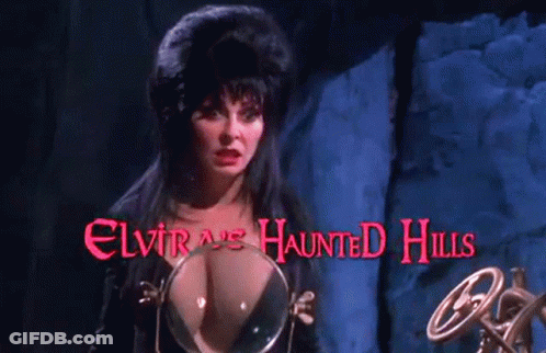 A Woman Stands In Front Of A Sign That Says Elvira 'S Haunted Hills On It GIF
