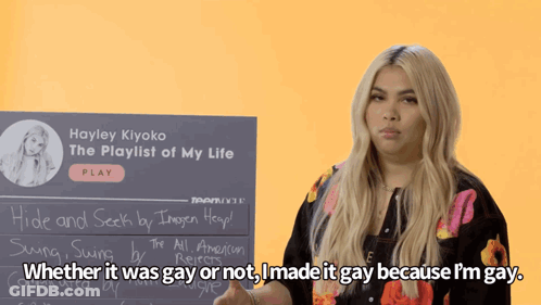 A Woman Stands In Front Of A Sign That Says Hayley Kiyoko The Playlist Of My Life GIF