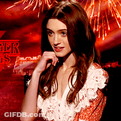 A Woman Stands In Front Of A Sign That Says Stranger Things On It GIF