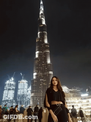 A Woman Stands In Front Of A Very Tall Building GIF