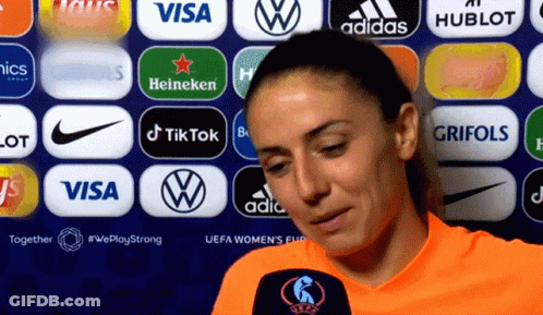 A Woman Stands In Front Of A Wall Of Logos Including Visa And Adidas GIF