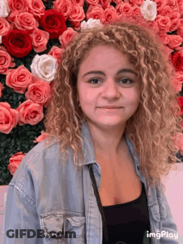 A Woman Stands In Front Of A Wall Of Pink Roses GIF