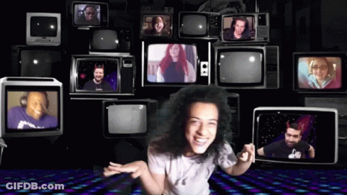 A Woman Stands In Front Of A Wall Of Televisions Including One That Says S2 On It GIF