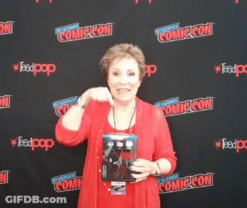 A Woman Stands In Front Of A Wall That Says Comic Con On It GIF