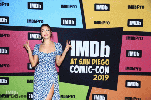A Woman Stands In Front Of A Wall That Says Imdb At San Diego Comic Con GIF