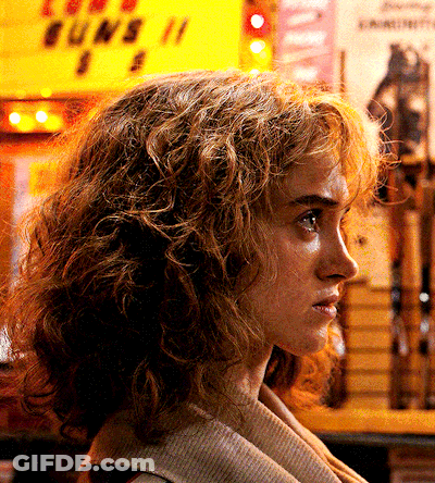 A Woman Stands In Front Of A Yellow Sign That Says Guns GIF