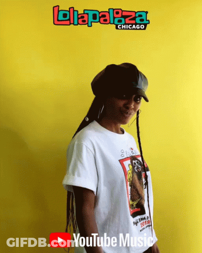 A Woman Stands In Front Of A Yellow Wall That Says ' Lolapaloza Chicago ' GIF