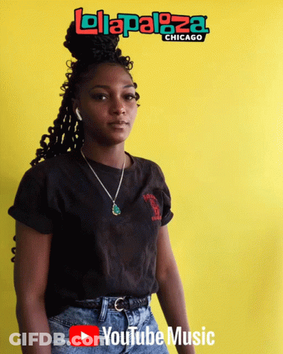 A Woman Stands In Front Of A Yellow Wall With A Lolapaloza Chicago Logo On It GIF