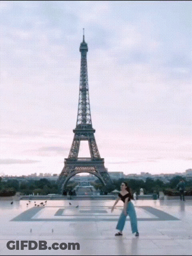 A Woman Stands In Front Of The Eiffel Tower In Paris GIF