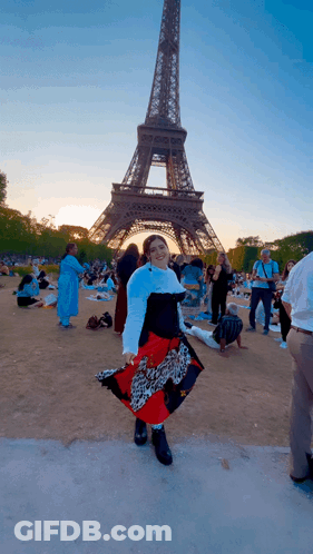 A Woman Stands In Front Of The Eiffel Tower Wearing A Leopard Print Skirt GIF