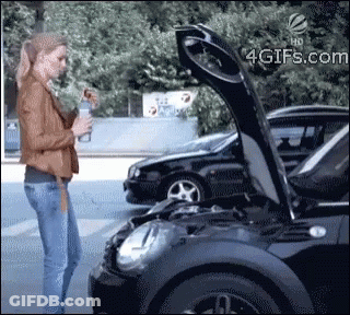 A Woman Stands Next To A Black Car With The Hood Open GIF