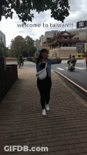 A Woman Stands On A Brick Sidewalk With Her Arms Outstretched And The Words Welcome To Taiwan Written Below Her GIF