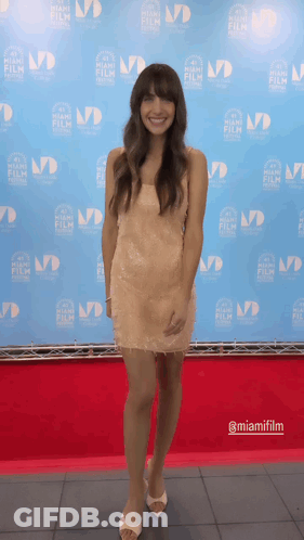 A Woman Stands On A Red Carpet In Front Of A Backdrop That Says Miamifilm GIF