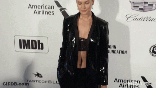 A Woman Stands On A Red Carpet In Front Of An Imdb Logo GIF