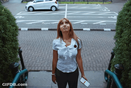 A Woman Stands On A Set Of Stairs Looking Up At A Parking Lot With A White Car Parked In It GIF