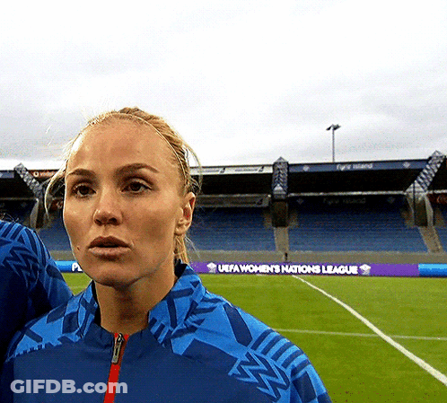 A Woman Stands On A Soccer Field With A Uefa Women 'S Nations League Banner In The Background GIF