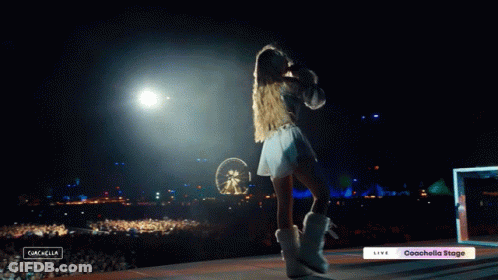 A Woman Stands On A Stage In Front Of A Crowd With A Sign That Says Coachella Stage GIF