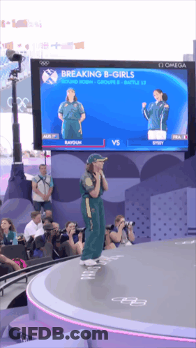 A Woman Stands On A Stage In Front Of A Large Screen Which Says Breaking B-Girls GIF