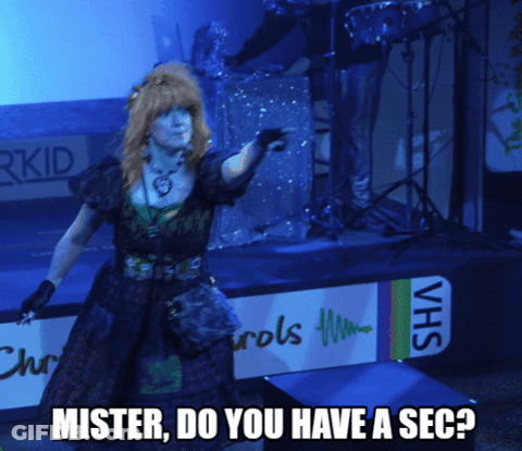 A Woman Stands On A Stage With A Sign That Says Vhs GIF