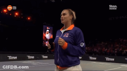 A Woman Stands On A Tennis Court Wearing A Blue And Orange Jacket GIF