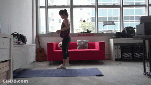 A Woman Stands On A Yoga Mat In Front Of A Red Couch And A Sign That Says Walk On The Side GIF