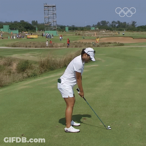A Woman Swinging A Golf Club On A Golf Course With The Olympic Rings In The Background GIF