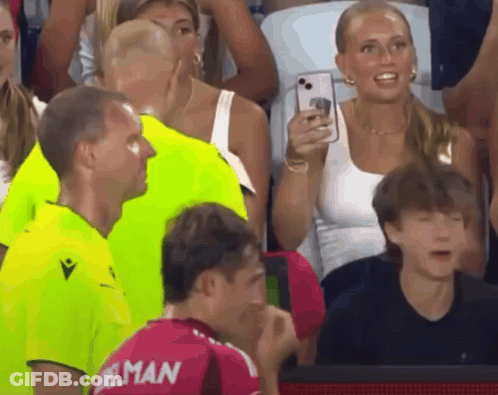 A Woman Takes A Picture Of A Man Wearing A Jersey That Says ' Elman ' On It GIF
