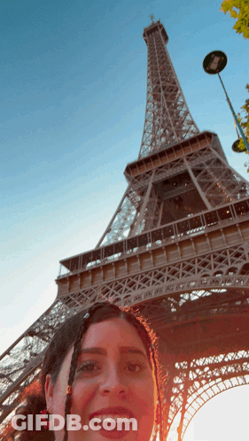 A Woman Taking A Picture In Front Of The Eiffel Tower GIF