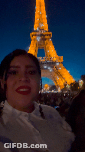 A Woman Taking A Picture In Front Of The Eiffel Tower At Night GIF