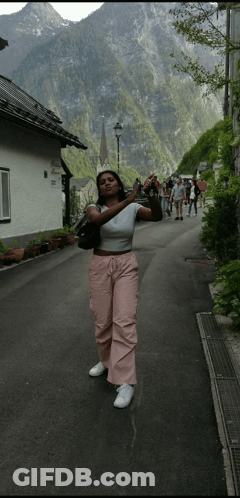 A Woman Taking A Picture Of A Mountain While Standing On A Street GIF