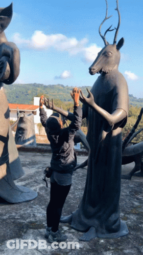 A Woman Taking A Picture Of A Statue With A Deer Head GIF