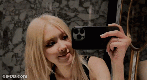 A Woman Taking A Picture Of Herself In A Mirror With Her Phone GIF
