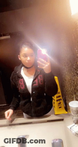 A Woman Taking A Selfie In Front Of A Mirror With A Yellow Caution Sign In The Background GIF