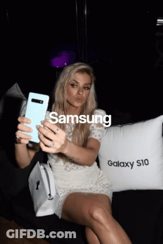 A Woman Taking A Selfie Next To A Pillow That Says Samsung GIF