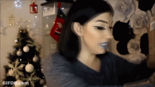 A Woman Taking A Selfie With A Christmas Tree In The Background GIF
