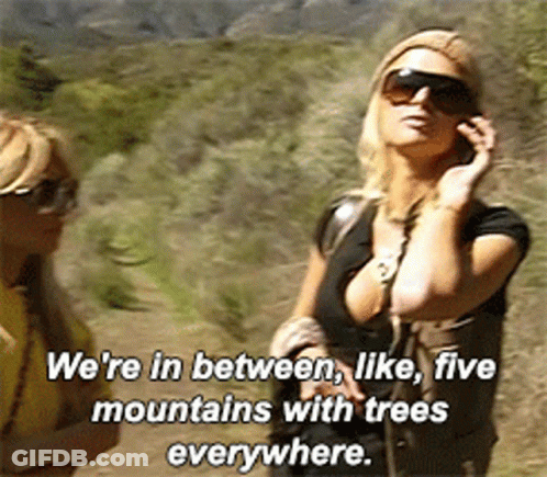 A Woman Talking On A Cell Phone With The Words We 'Re In Between Like Five Mountains With Trees Everywhere Above Her GIF